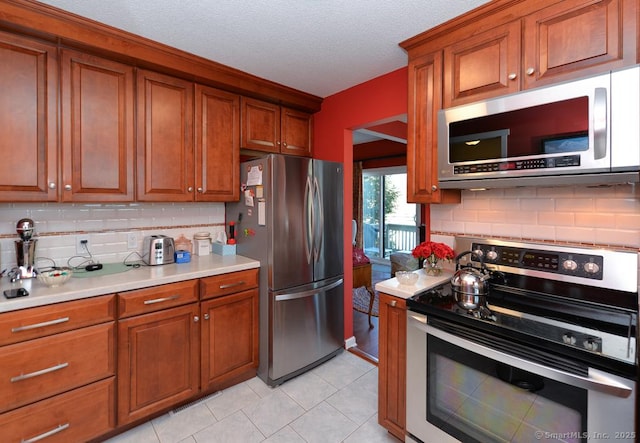 kitchen with decorative backsplash, light tile patterned floors, stainless steel appliances, and a textured ceiling