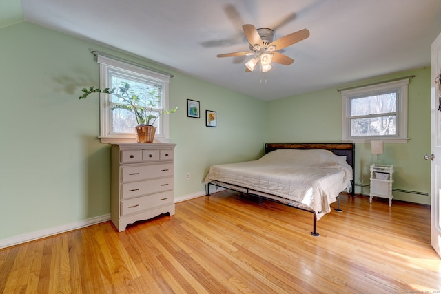 bedroom with ceiling fan, light hardwood / wood-style floors, a baseboard radiator, and multiple windows