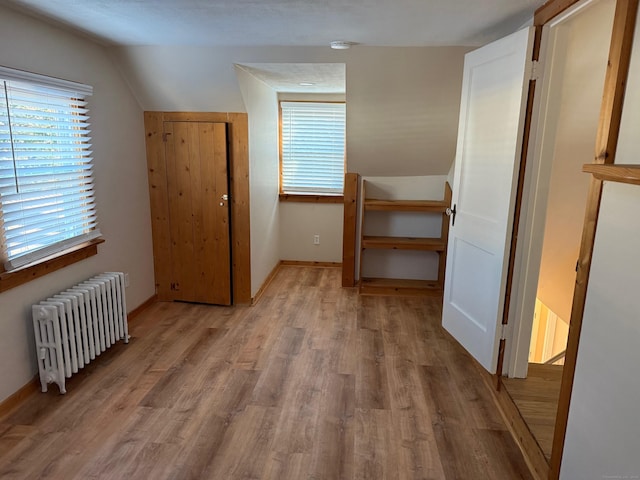 additional living space featuring light wood-type flooring, lofted ceiling, and radiator