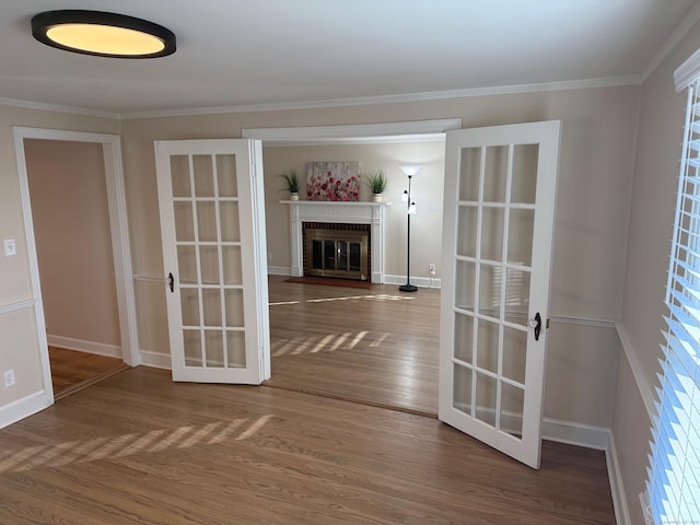 unfurnished room with french doors, wood-type flooring, ornamental molding, and a brick fireplace