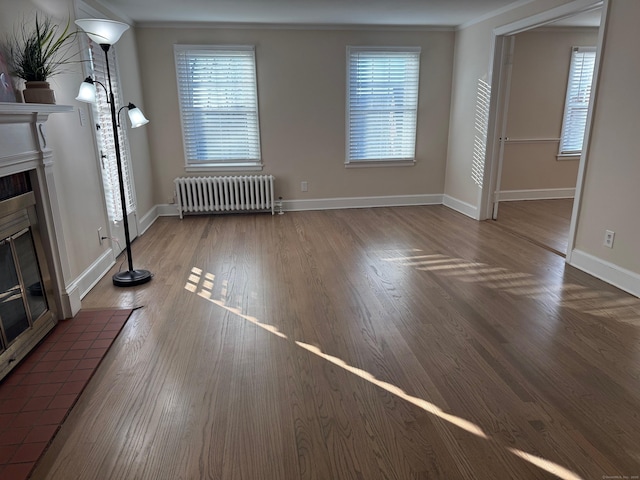 unfurnished living room featuring a tiled fireplace, crown molding, radiator heating unit, and hardwood / wood-style floors