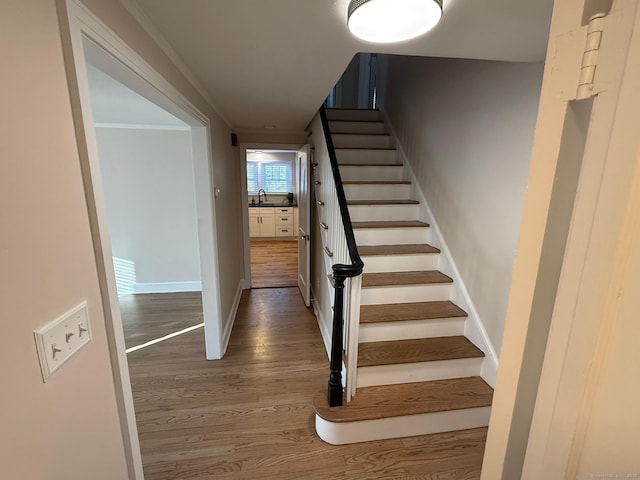 staircase with crown molding, sink, and wood-type flooring