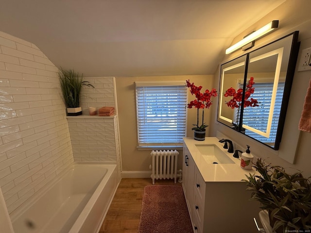 bathroom featuring vanity, radiator, vaulted ceiling, hardwood / wood-style flooring, and a tub