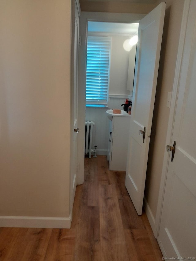 hallway with radiator heating unit, light hardwood / wood-style floors, and sink