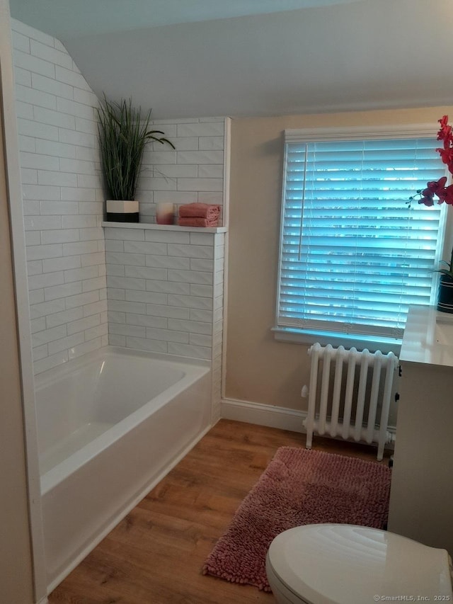 bathroom featuring vaulted ceiling, a bath, wood-type flooring, radiator heating unit, and toilet