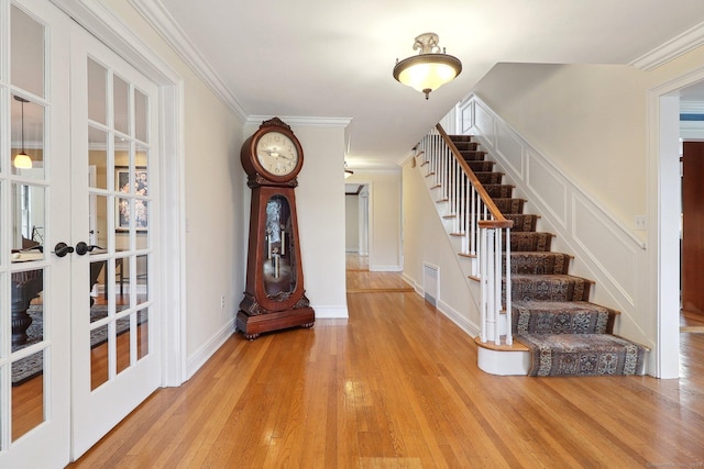 foyer entrance with light wood-type flooring, ornamental molding, and french doors