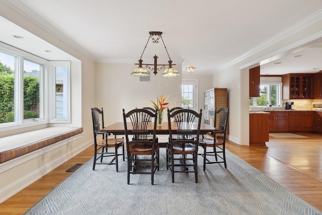 dining area featuring light wood-type flooring, crown molding, and a wealth of natural light