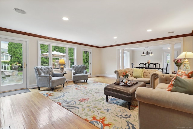 living room featuring a chandelier, light wood-type flooring, decorative columns, and ornamental molding