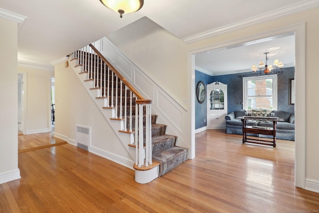 stairs with crown molding, hardwood / wood-style floors, and an inviting chandelier