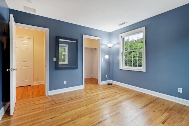 unfurnished bedroom featuring a walk in closet, light hardwood / wood-style flooring, and multiple windows