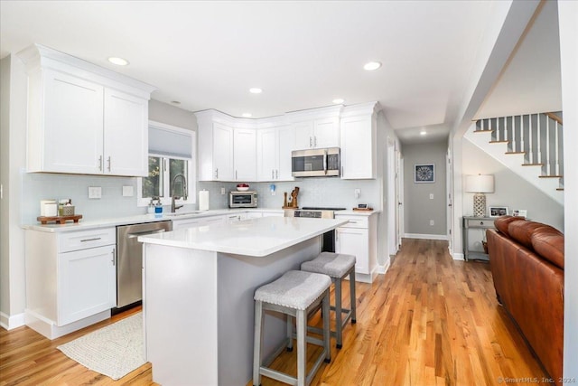 kitchen with a breakfast bar, stainless steel appliances, white cabinets, light hardwood / wood-style floors, and a kitchen island