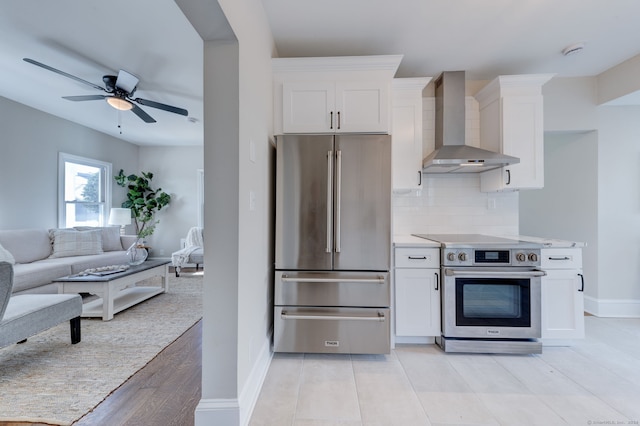 kitchen with decorative backsplash, appliances with stainless steel finishes, wall chimney exhaust hood, ceiling fan, and white cabinets