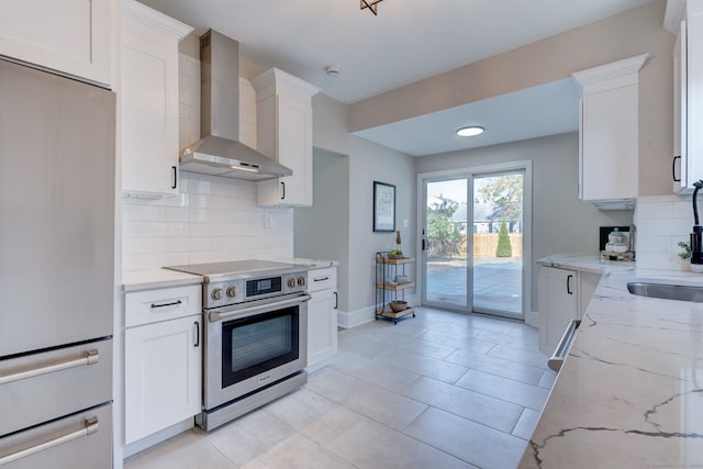 kitchen with light stone countertops, appliances with stainless steel finishes, tasteful backsplash, wall chimney exhaust hood, and white cabinetry