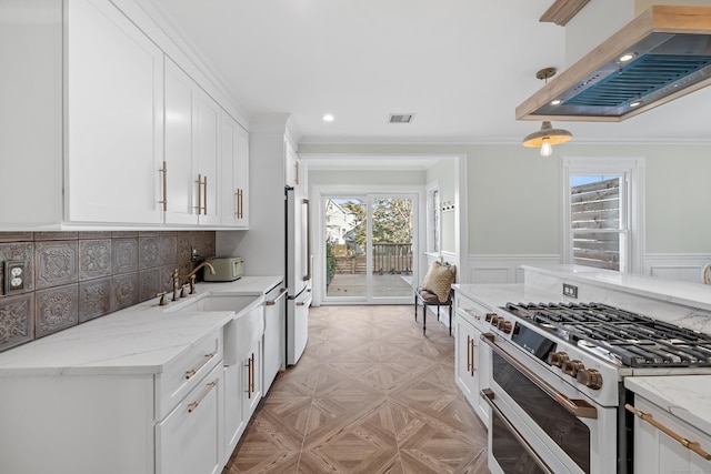 kitchen with a wealth of natural light, high quality appliances, white cabinetry, exhaust hood, and light stone counters