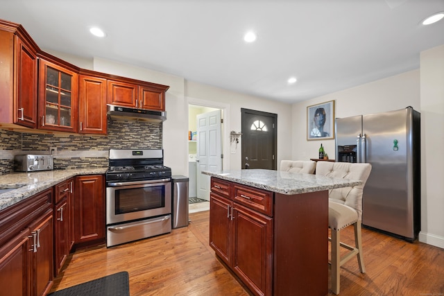 kitchen featuring light hardwood / wood-style floors, stainless steel appliances, light stone countertops, and a breakfast bar area