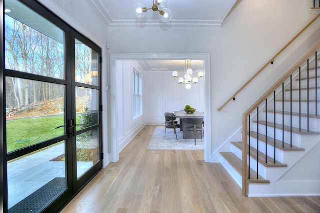 interior space featuring crown molding, french doors, light wood-type flooring, and a notable chandelier