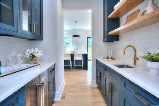 kitchen featuring pendant lighting, backsplash, blue cabinets, and sink