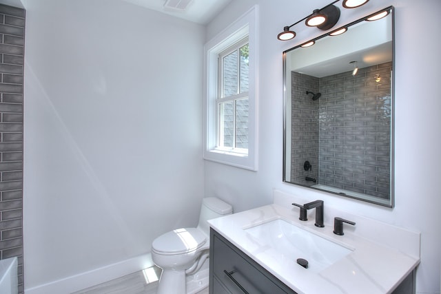 bathroom with a tile shower, plenty of natural light, vanity, and toilet