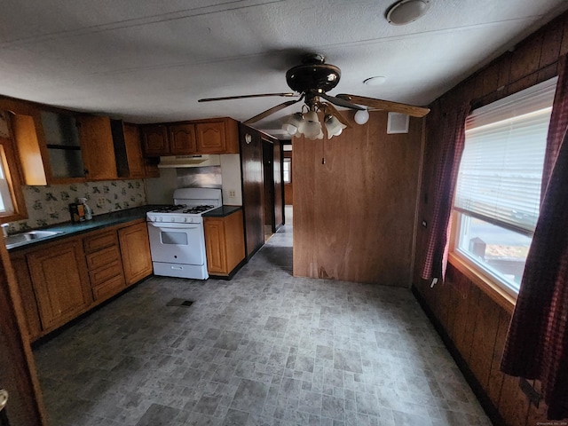 kitchen with white range with gas cooktop, ceiling fan, sink, and wood walls