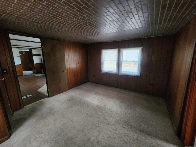 unfurnished room featuring wood walls, brick ceiling, and light carpet