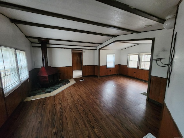 unfurnished living room featuring lofted ceiling with beams, a wood stove, plenty of natural light, and dark wood-type flooring