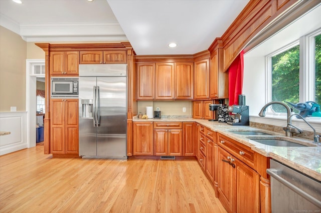 kitchen with light stone countertops, sink, built in appliances, crown molding, and light hardwood / wood-style floors