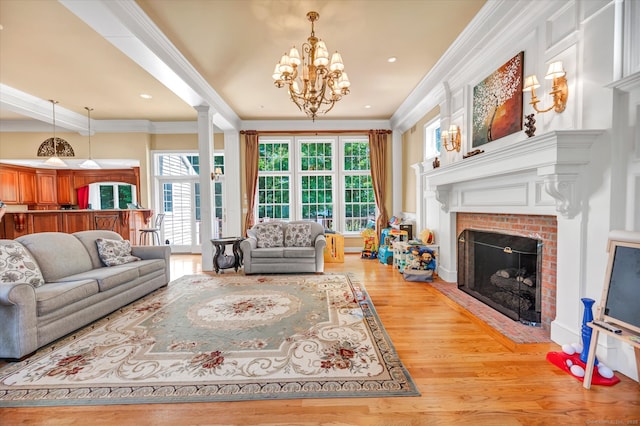 living room with hardwood / wood-style floors, a chandelier, crown molding, and a brick fireplace