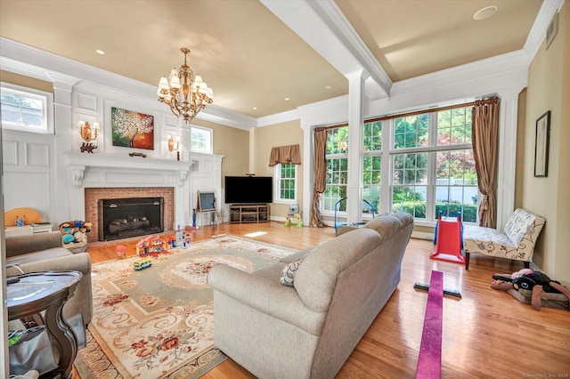 living room with decorative columns, ornamental molding, light hardwood / wood-style flooring, a fireplace, and a chandelier