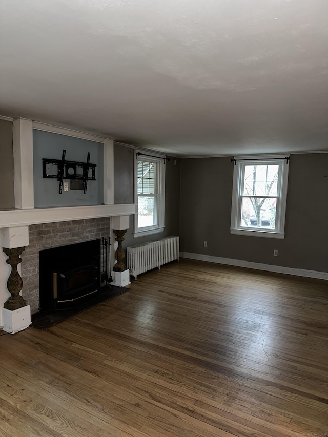 unfurnished living room featuring wood-type flooring, a brick fireplace, a wealth of natural light, and radiator heating unit