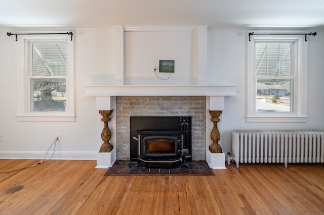 interior details with wood finished floors, baseboards, ornamental molding, radiator heating unit, and a wood stove