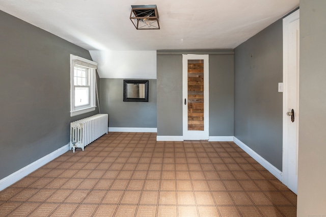 empty room with baseboards, tile patterned floors, lofted ceiling, and radiator