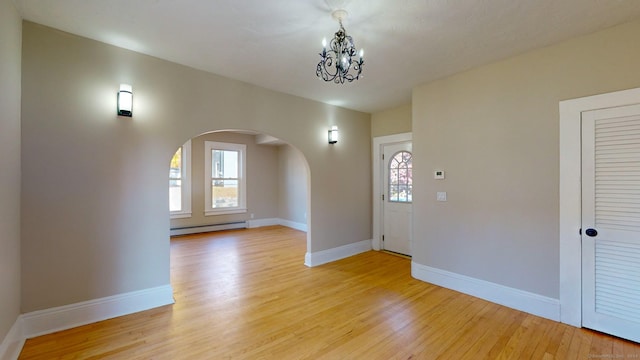 interior space with a notable chandelier, a healthy amount of sunlight, baseboard heating, and light hardwood / wood-style flooring