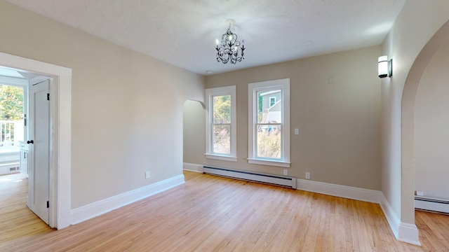 empty room with a chandelier, light hardwood / wood-style floors, plenty of natural light, and a baseboard heating unit