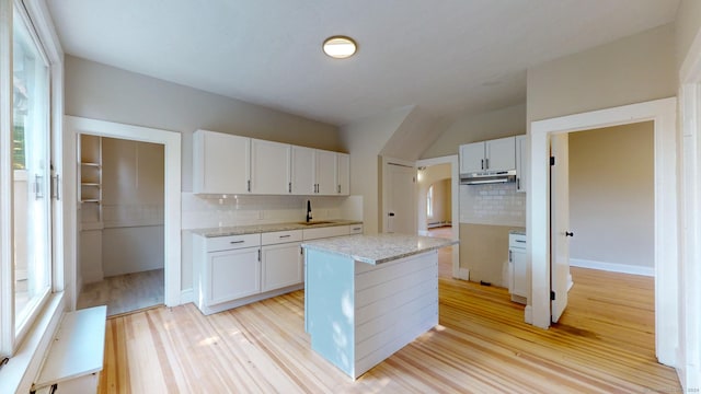 kitchen with white cabinets, decorative backsplash, a kitchen island, and light hardwood / wood-style floors