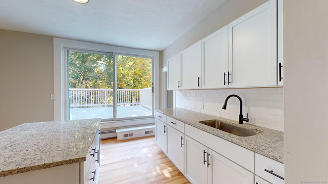 kitchen featuring backsplash, a baseboard heating unit, sink, light stone counters, and white cabinetry