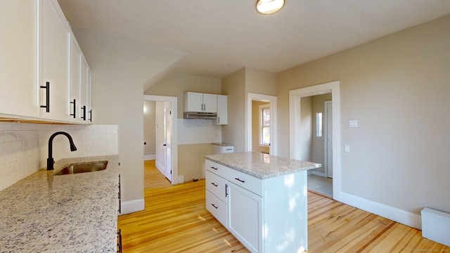 kitchen featuring sink, decorative backsplash, a kitchen island, light stone counters, and white cabinetry