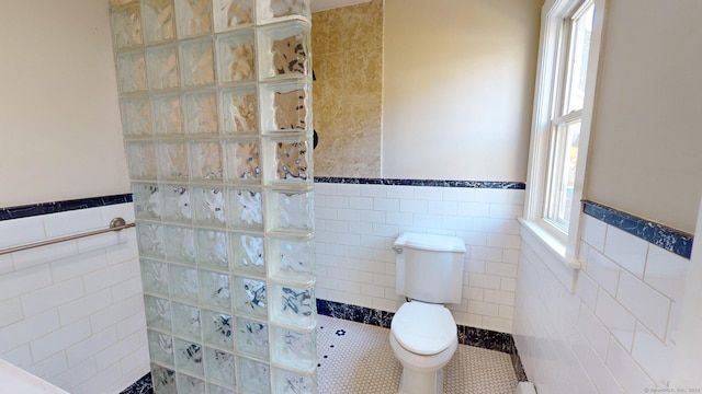 bathroom with a shower, tile patterned flooring, tile walls, and toilet