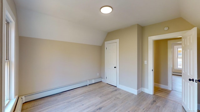 additional living space featuring lofted ceiling, light hardwood / wood-style floors, and a baseboard heating unit