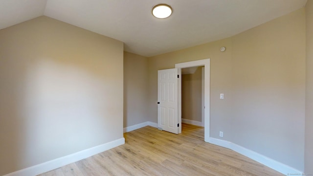 empty room with light hardwood / wood-style floors and vaulted ceiling