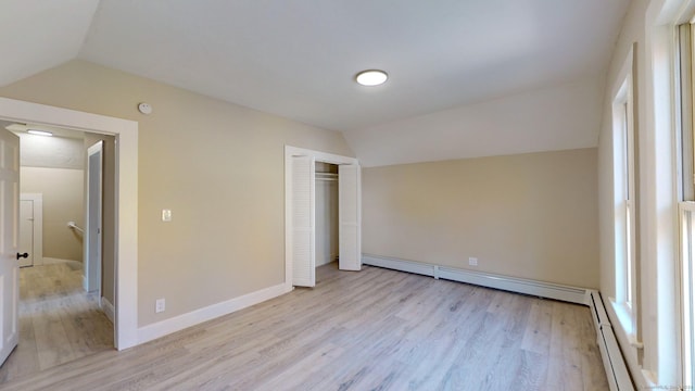 unfurnished bedroom featuring lofted ceiling, light hardwood / wood-style flooring, a baseboard radiator, and a closet