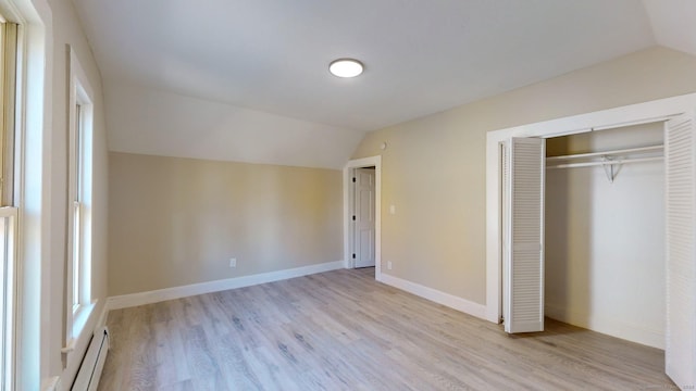 unfurnished bedroom with light wood-type flooring, baseboard heating, vaulted ceiling, and a closet