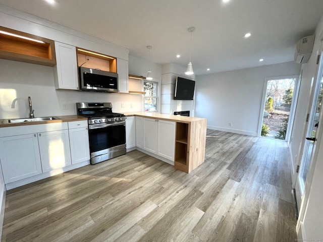 kitchen with appliances with stainless steel finishes, sink, an AC wall unit, white cabinetry, and hanging light fixtures