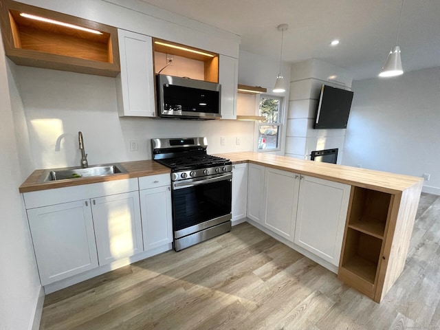 kitchen featuring butcher block counters, white cabinetry, sink, hanging light fixtures, and stainless steel appliances