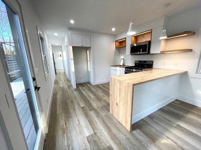 kitchen with gas stove, wood counters, decorative light fixtures, white cabinets, and light wood-type flooring