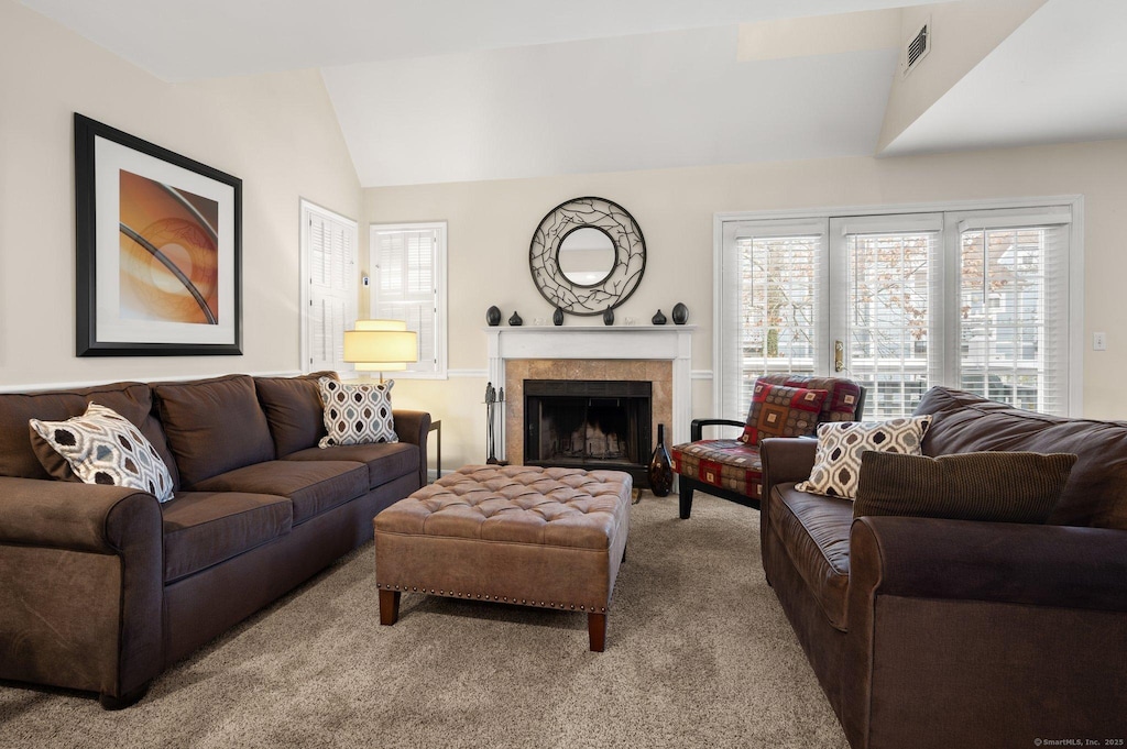 living room with a tile fireplace, light carpet, and lofted ceiling