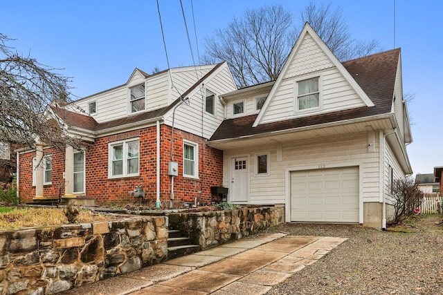 view of front of property featuring gravel driveway, an attached garage, a shingled roof, and brick siding