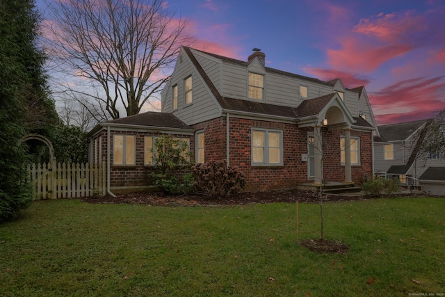 view of front of home featuring a front yard, brick siding, fence, and a chimney