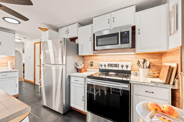 kitchen featuring white cabinets, dark tile patterned floors, light stone countertops, appliances with stainless steel finishes, and tasteful backsplash