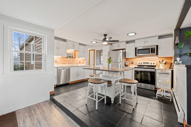 kitchen with backsplash, a breakfast bar area, baseboard heating, white cabinetry, and stainless steel appliances