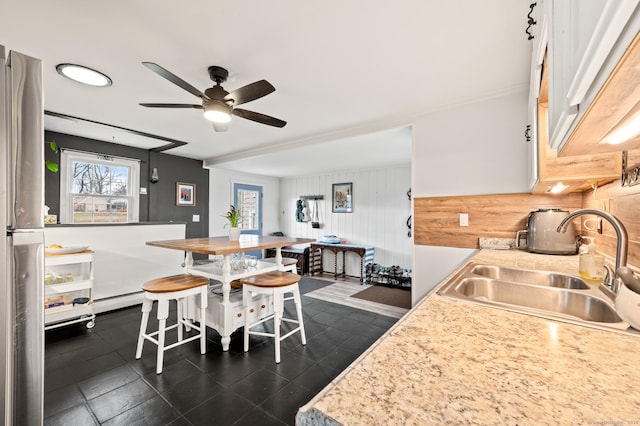 kitchen with a kitchen bar, stainless steel fridge, ceiling fan, wooden walls, and sink